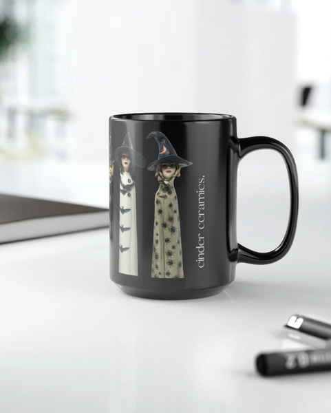 Black mug with witch design on a white surface, featuring the brand 'cinder ceramics'.