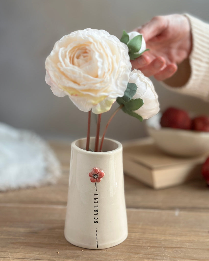 White flower arrangement in a small vase on a wooden surface with a blurred background