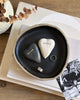 Heart-shaped stones with engraved names on a black dish, placed on a stack of books.
