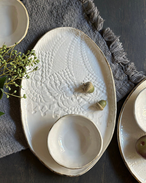 Set of white ceramic dishes with textured surface on a dark surface with green leaves.