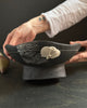 Person holding a black ceramic bowl with a white mushroom design on a dark surface