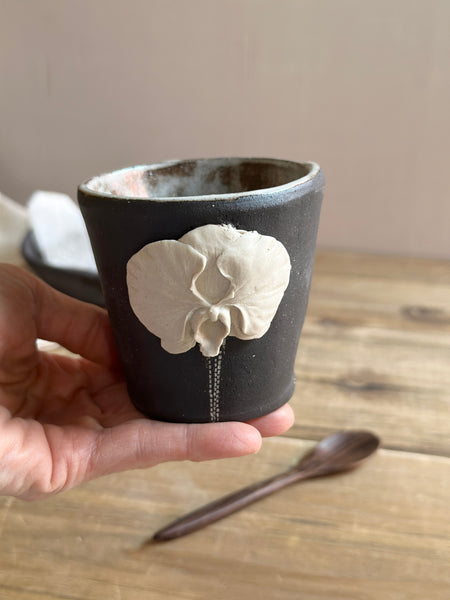 Ceramic cup with a floral design held by a hand on a wooden surface.
