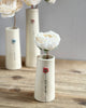 Three small ceramic vases with white flowers on a wooden surface.