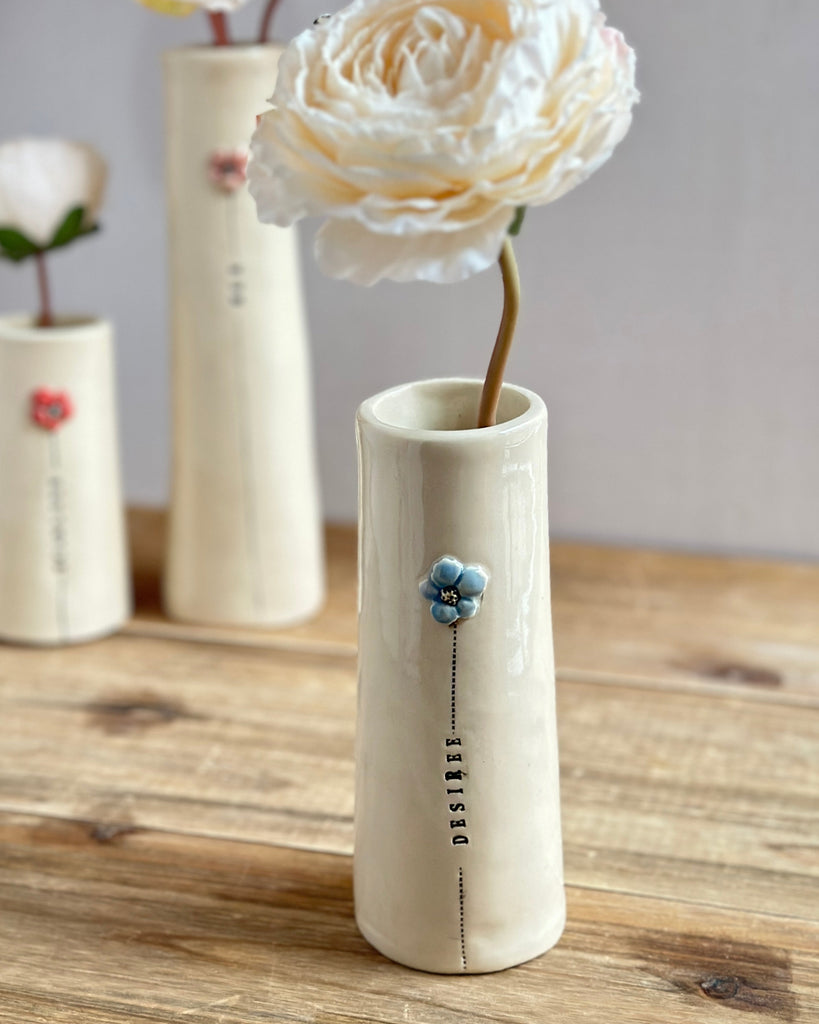 Three ceramic vases with flowers on a wooden surface