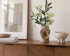 Decorative vase with flowers on a wooden surface next to a framed picture