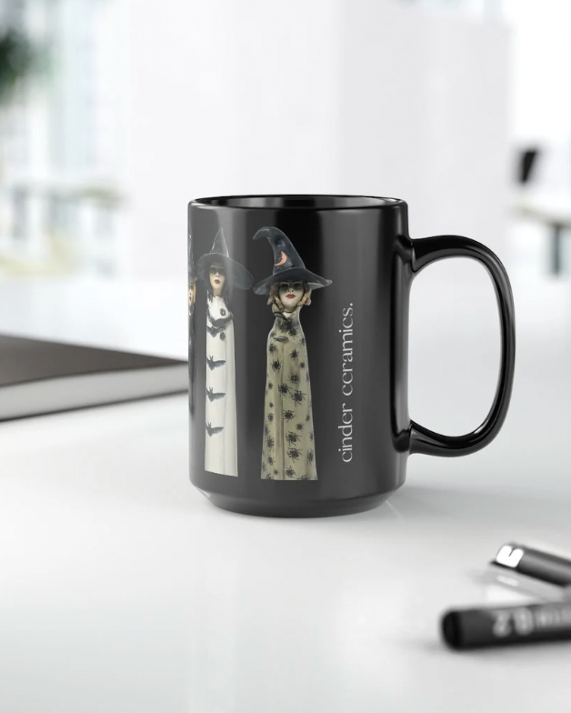 Black mug with witch design on a white surface, featuring the brand 'cinder ceramics'.
